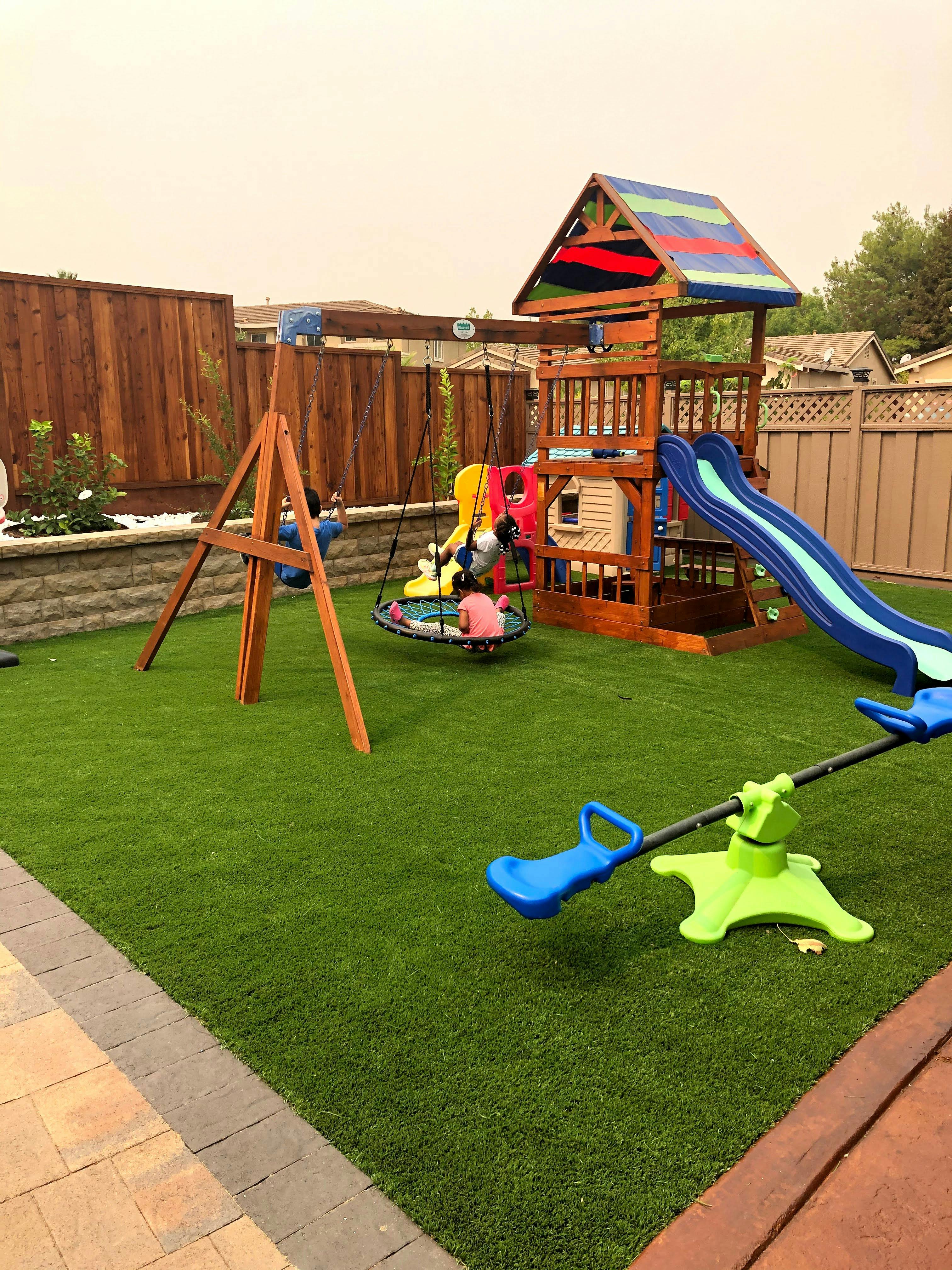Backyard playground with swing set, slide, and seesaw on artificial turf