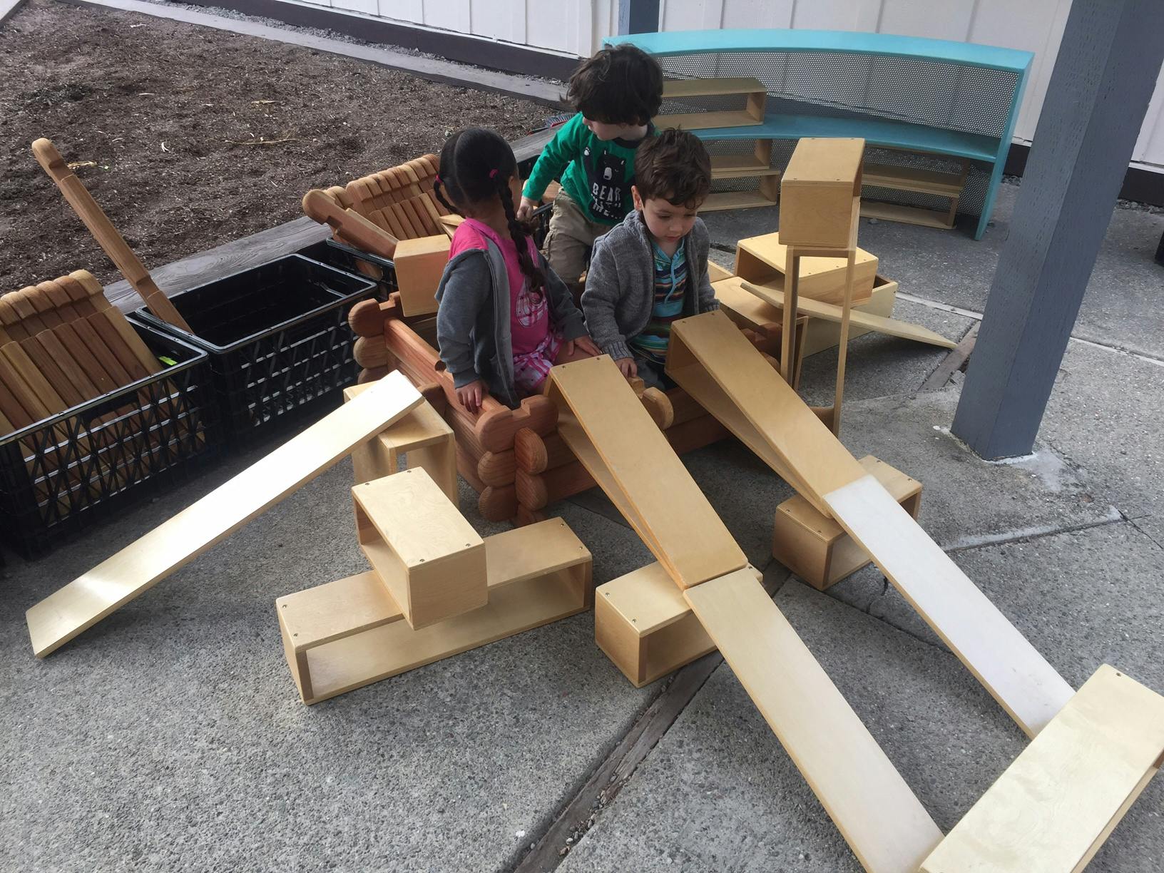 Three children playing with wooden blocks and ramps outdoors