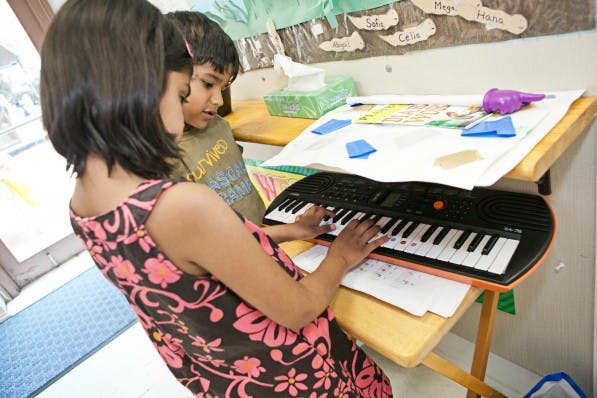 Person playing a keyboard with a child watching