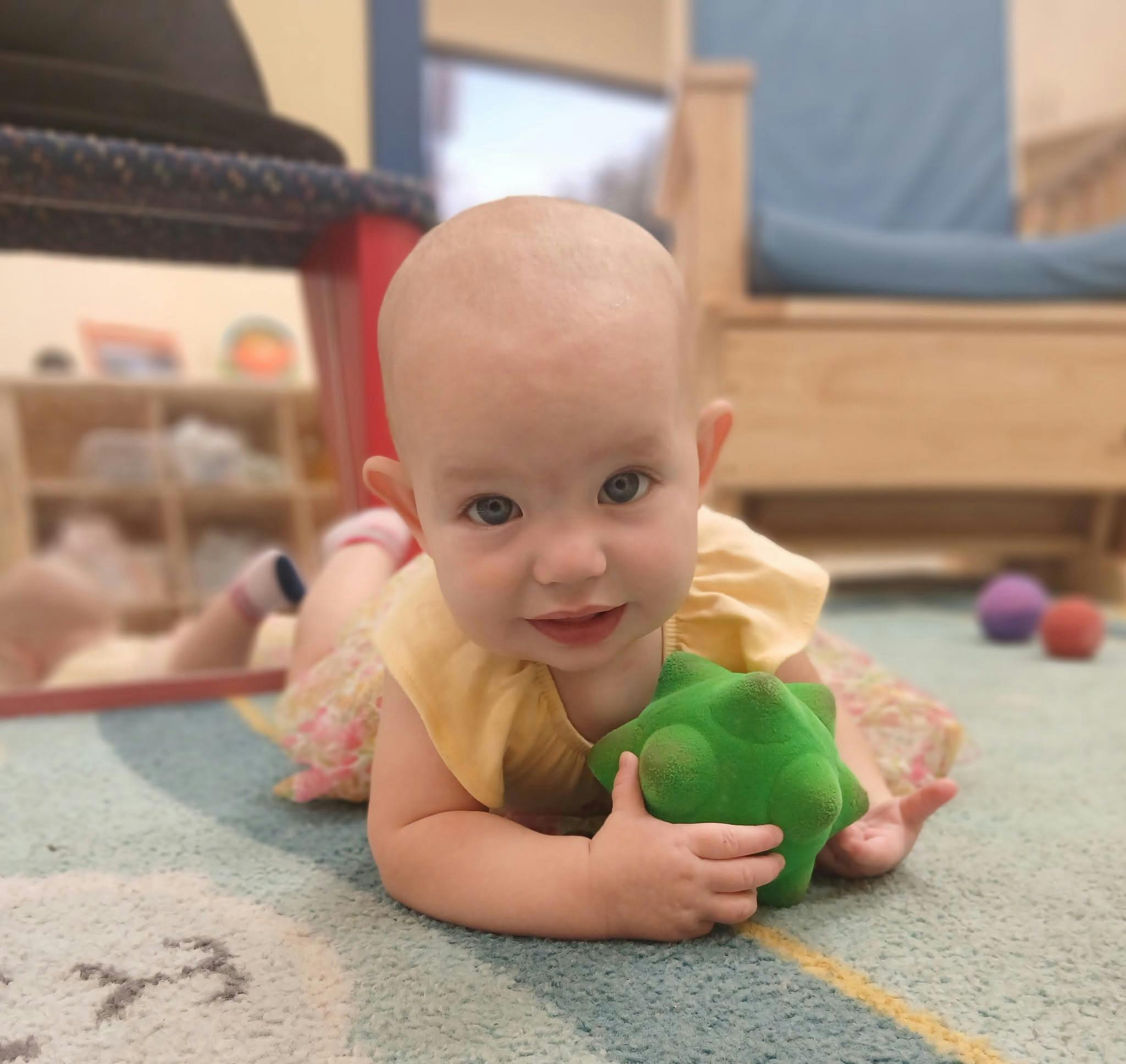 A baby lying on a carpet holding a green textured toy