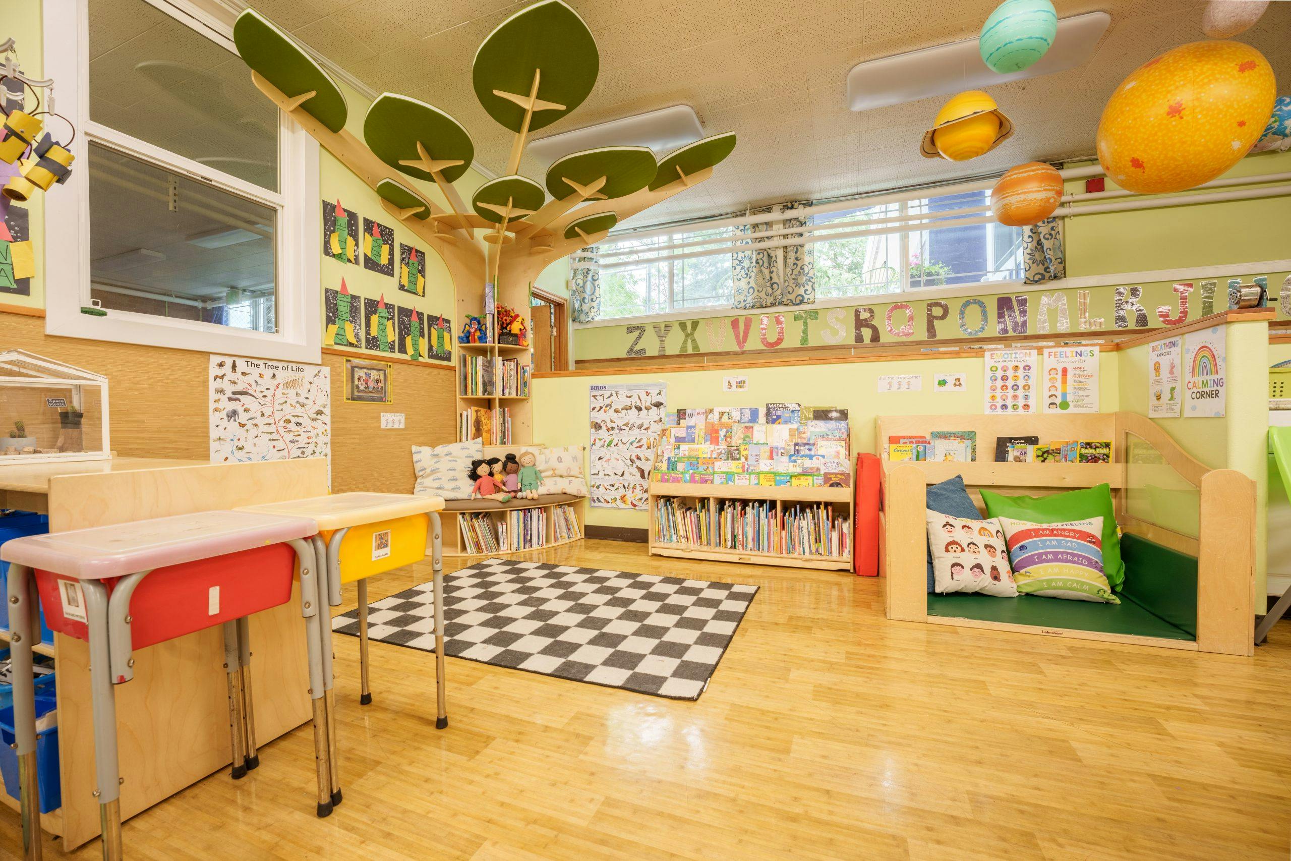 Classroom with child-sized desks, bookcases, reading nook, and educational posters