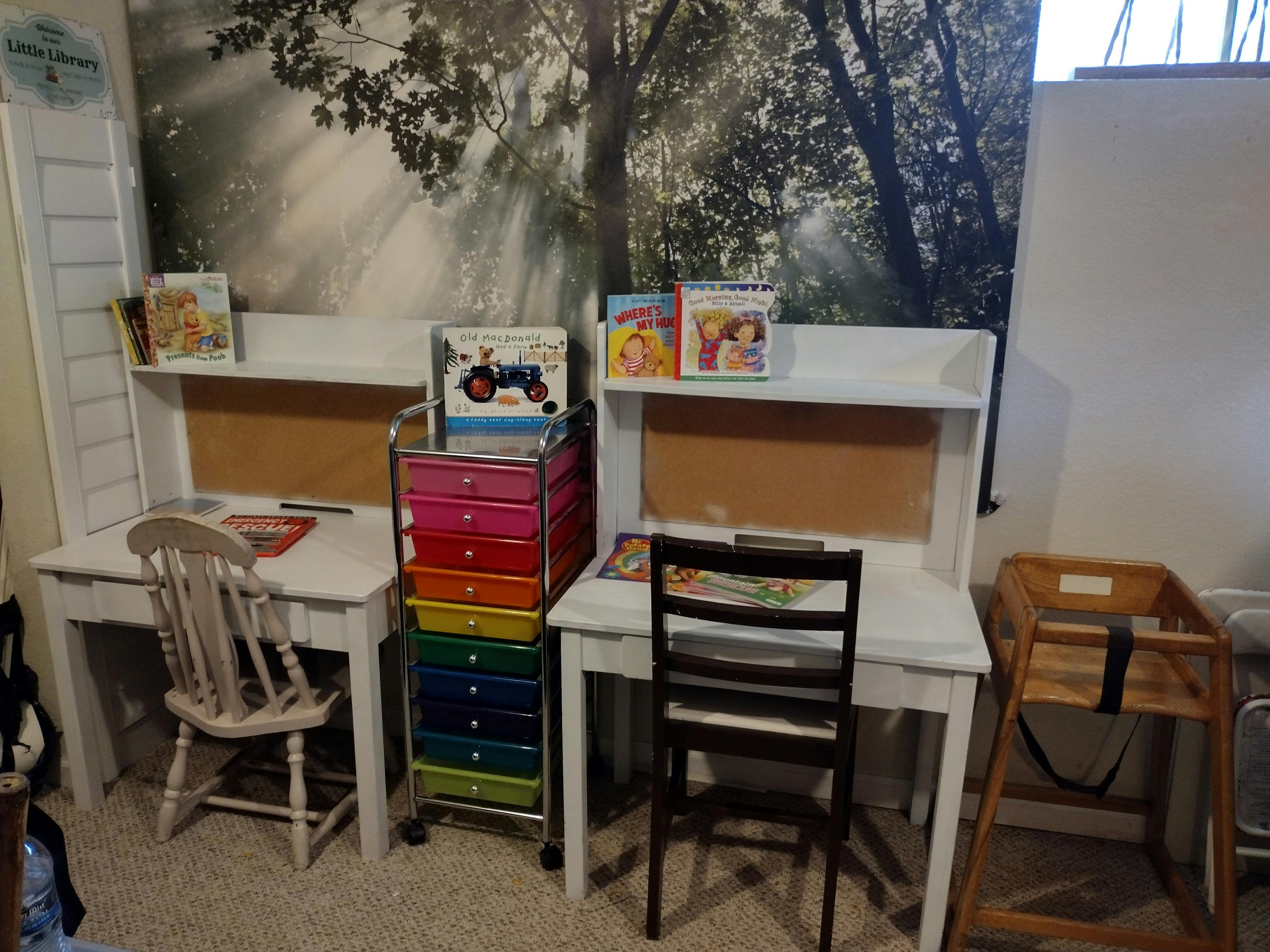Two white desks with chairs and books, colorful storage cart between them