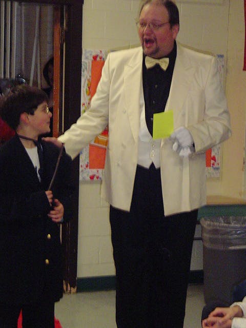 Person in a tuxedo with a child holding a wand