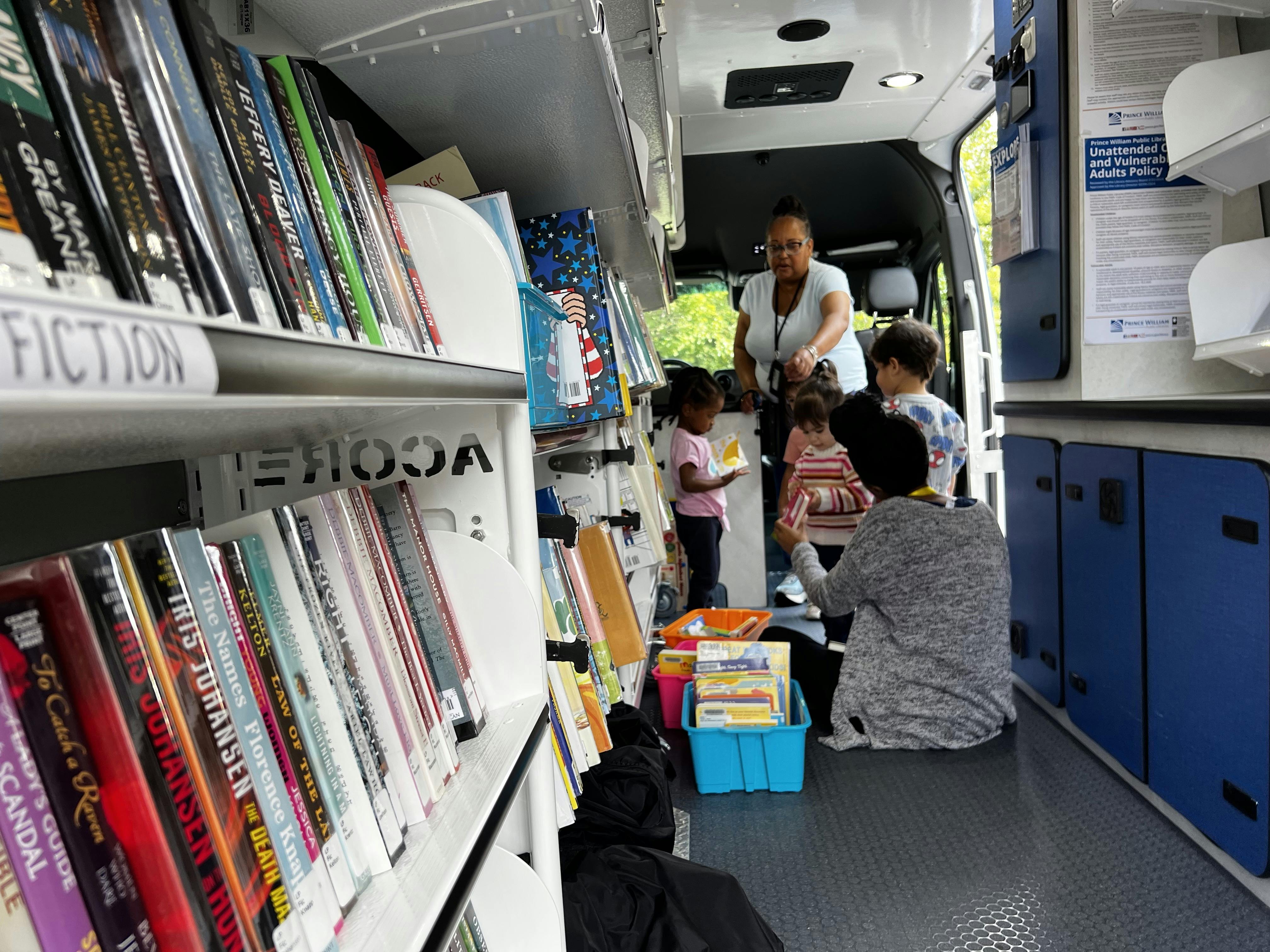 People and children inside a bookmobile with shelves of books