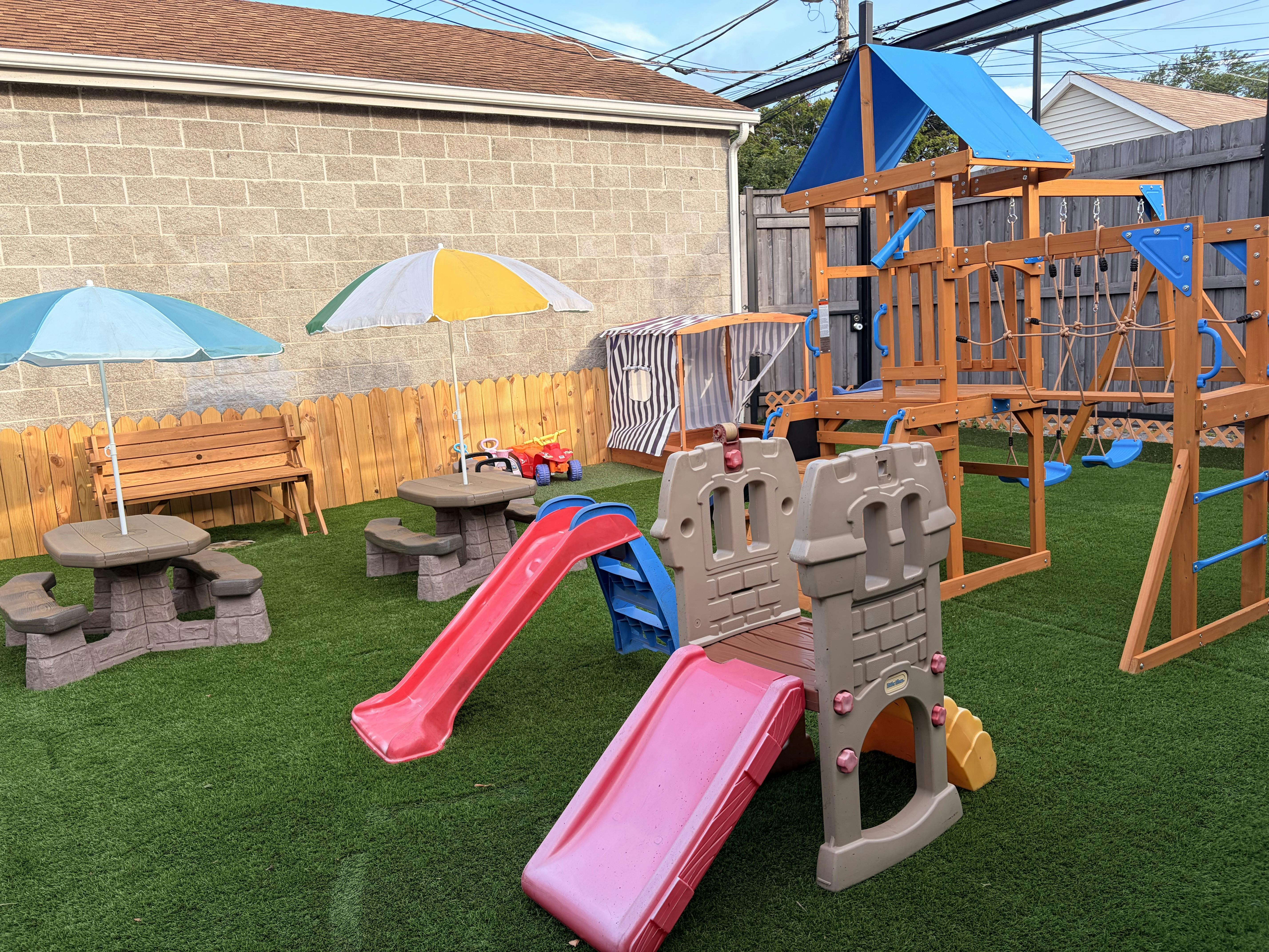 Childrens playground equipment and small tables with umbrellas on artificial turf