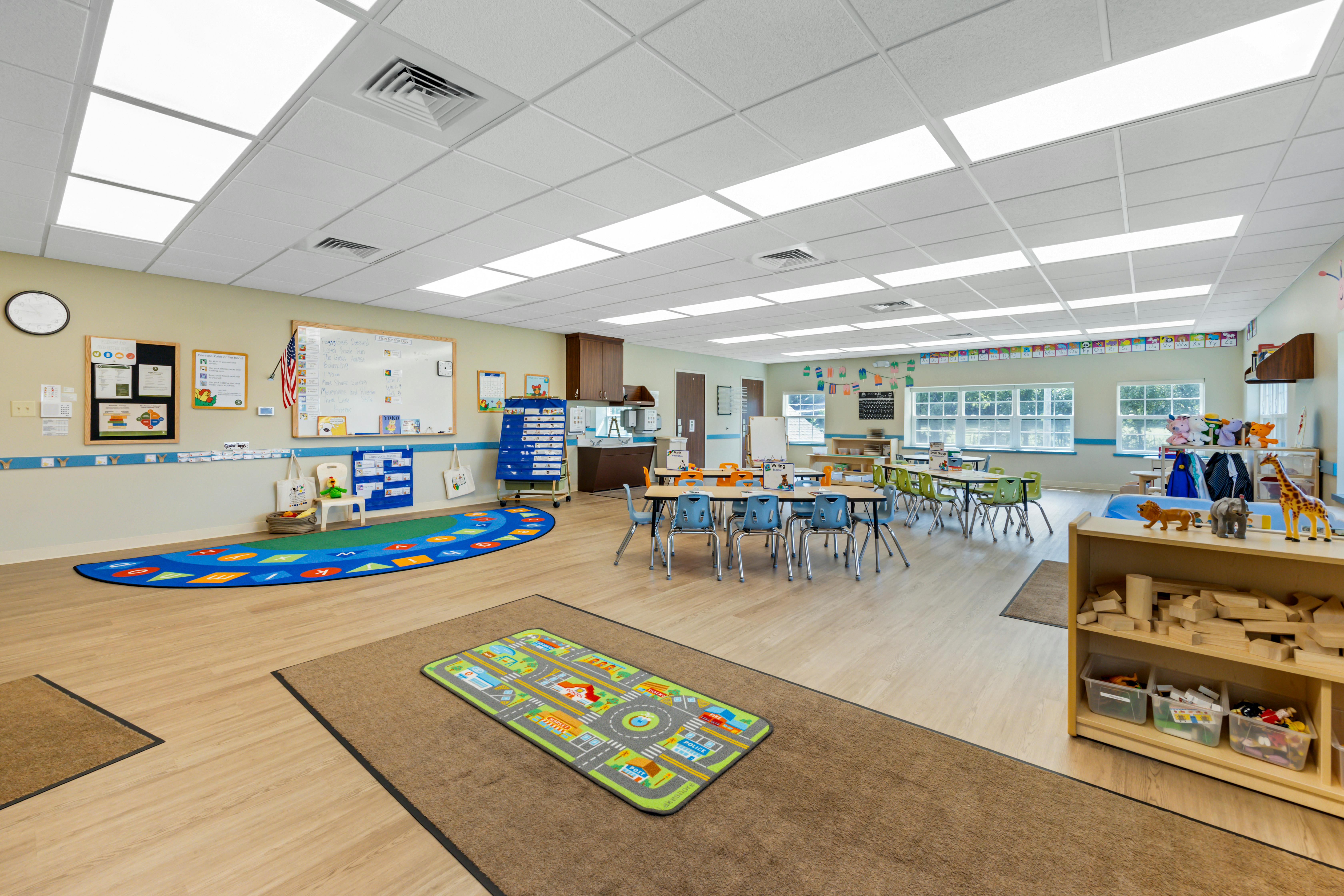 A brightly lit classroom with tables and chairs, play mats, and learning displays