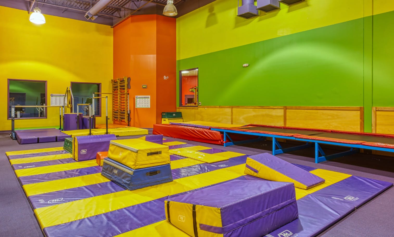 Colorful gymnastics room with mats, bars, and a long trampoline