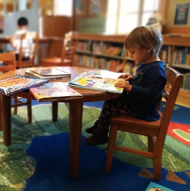 Child reading a book at a table in a library