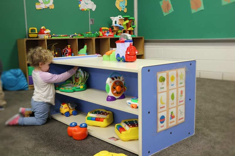 Child kneeling and reaching for a toy on a shelf in a classroom