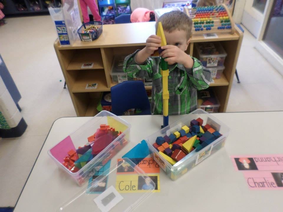 Child playing with building blocks at a table in a classroom