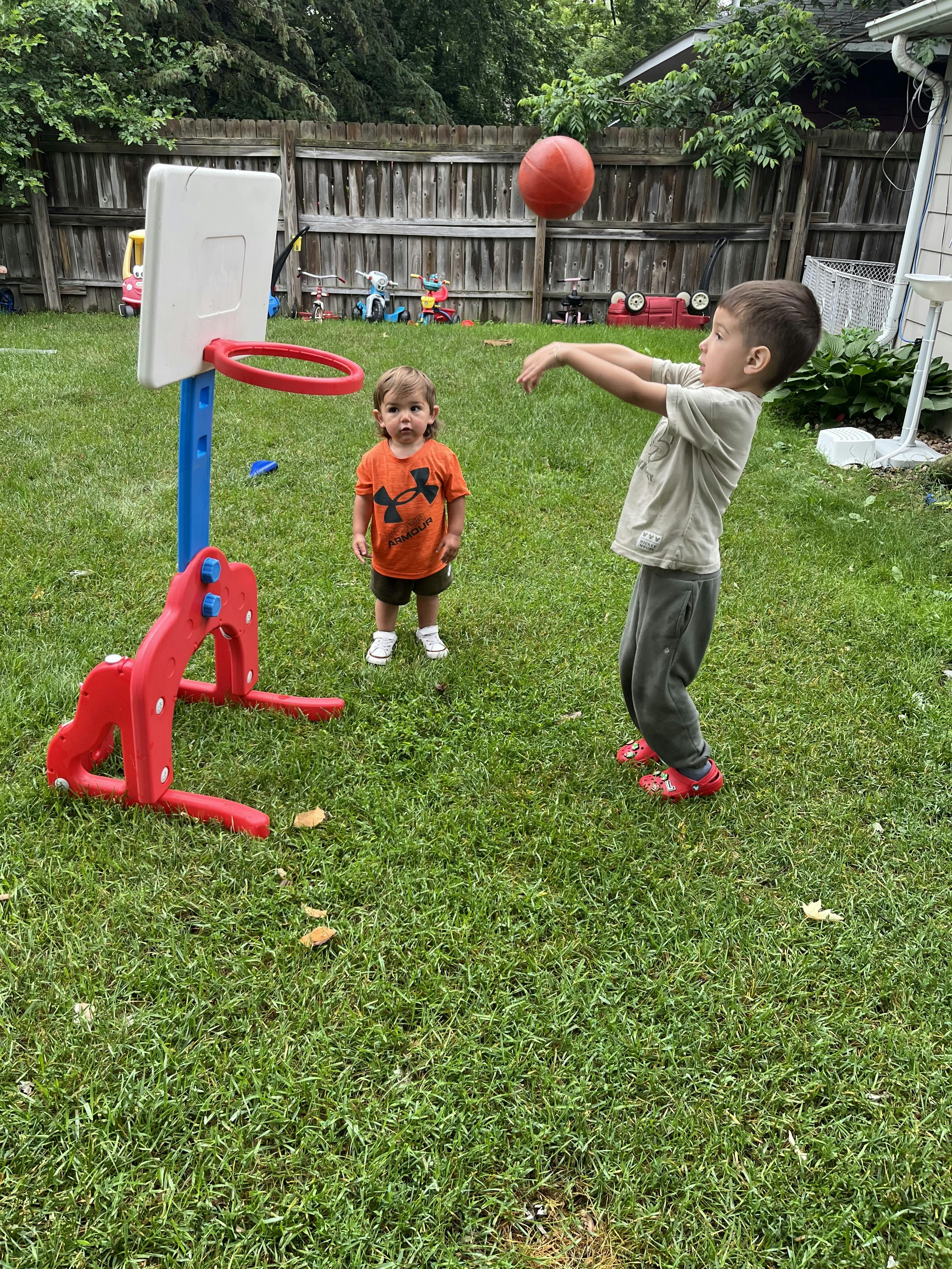 Two children playing basketball in a backyard