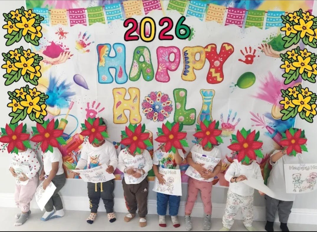 Children holding papers in front of a Happy Holi banner with 2026