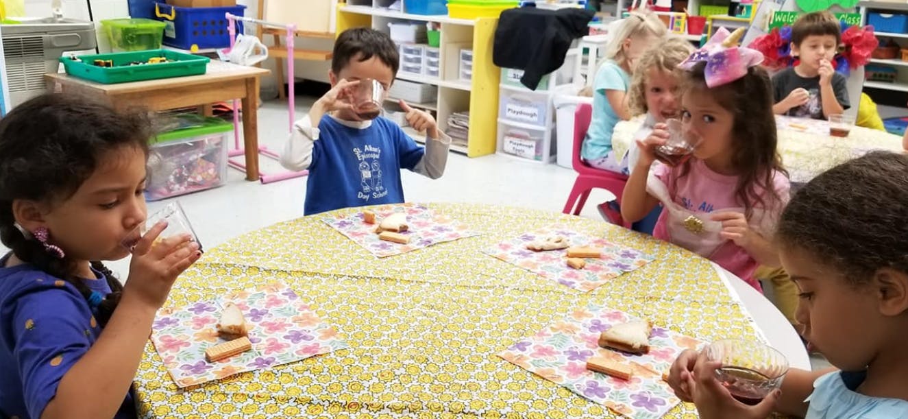 Children drinking from cups and eating snacks at a table in a classroom