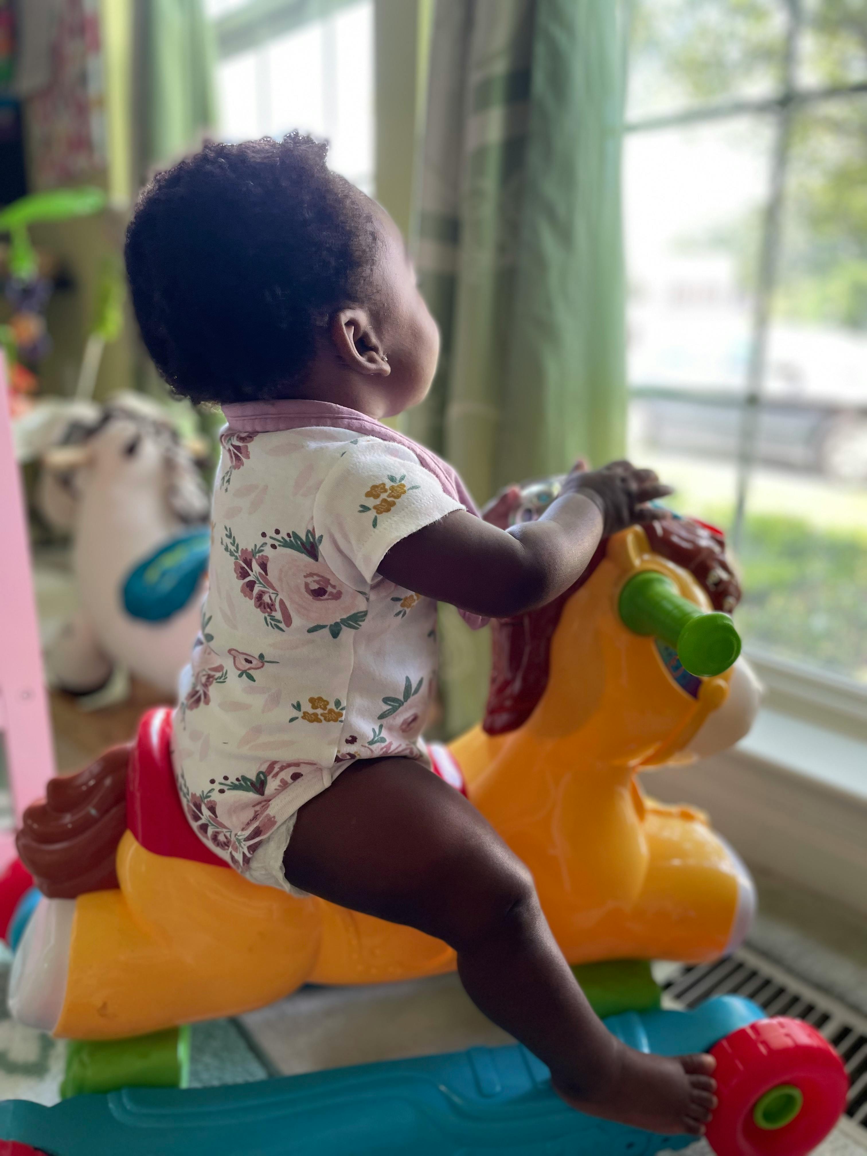Child on a toy horse looking out a window