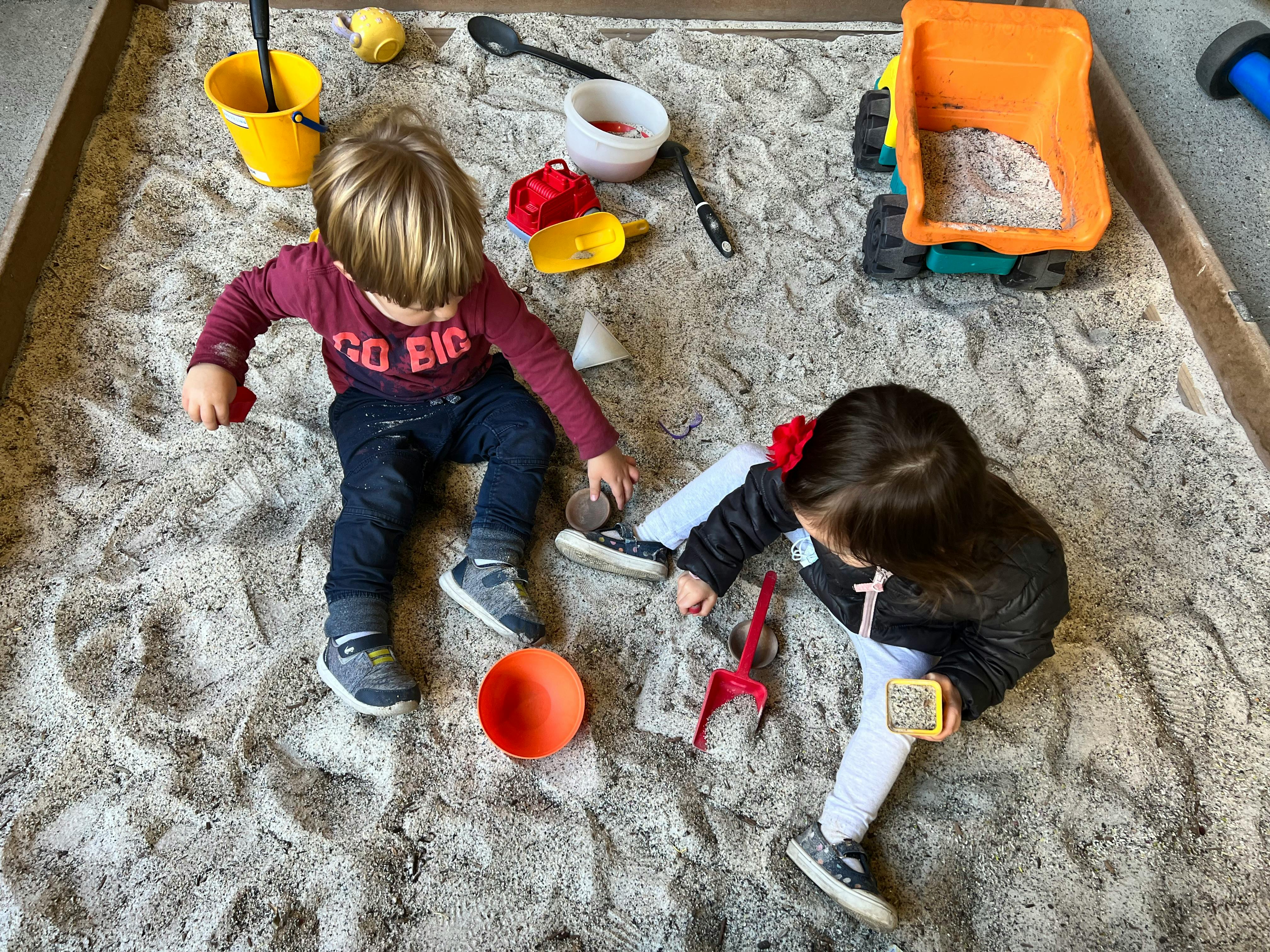 Two children playing in a sandbox with toys