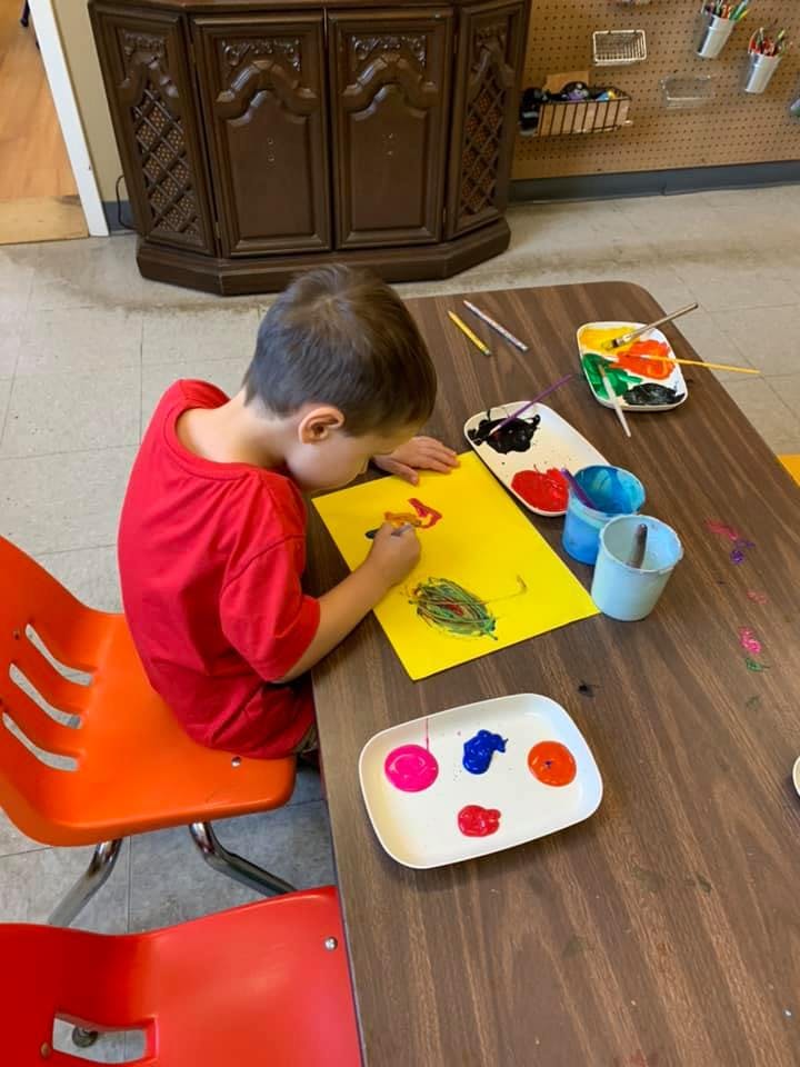 Child painting on yellow paper at a table