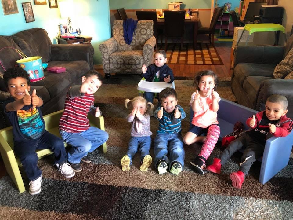 Group of children sitting on the floor and in chairs, some giving thumbs up