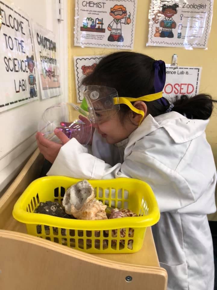 Child in lab coat and safety goggles looking into a container