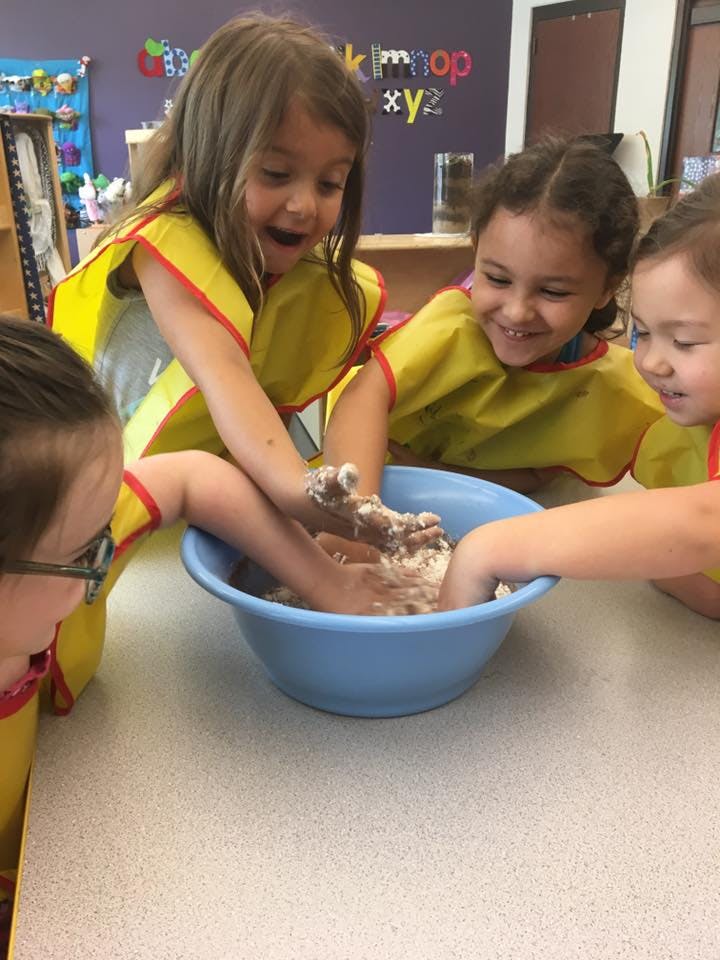 Children with aprons playing with dough in a blue bowl