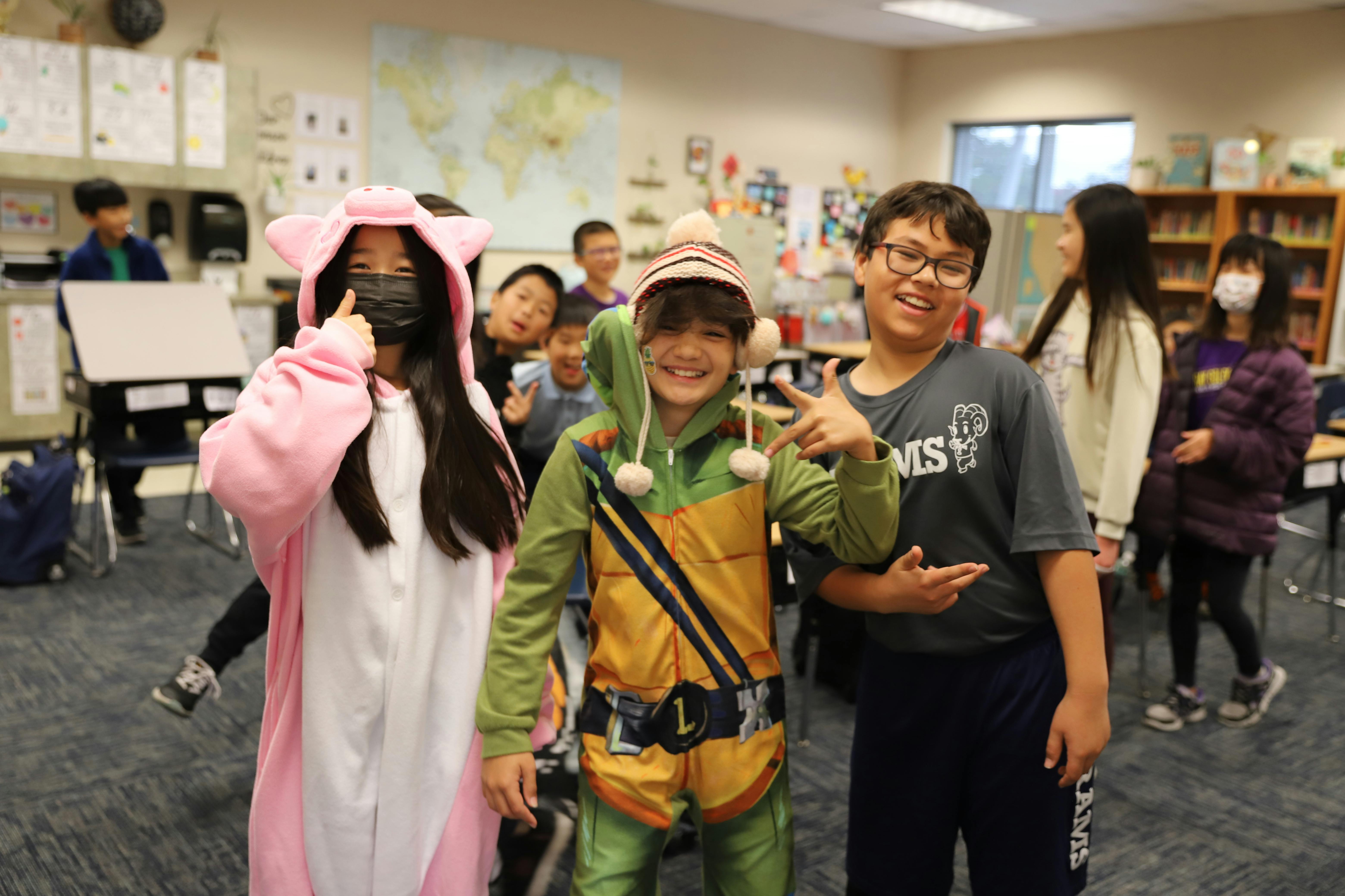 Three children in costumes posing in a classroom
