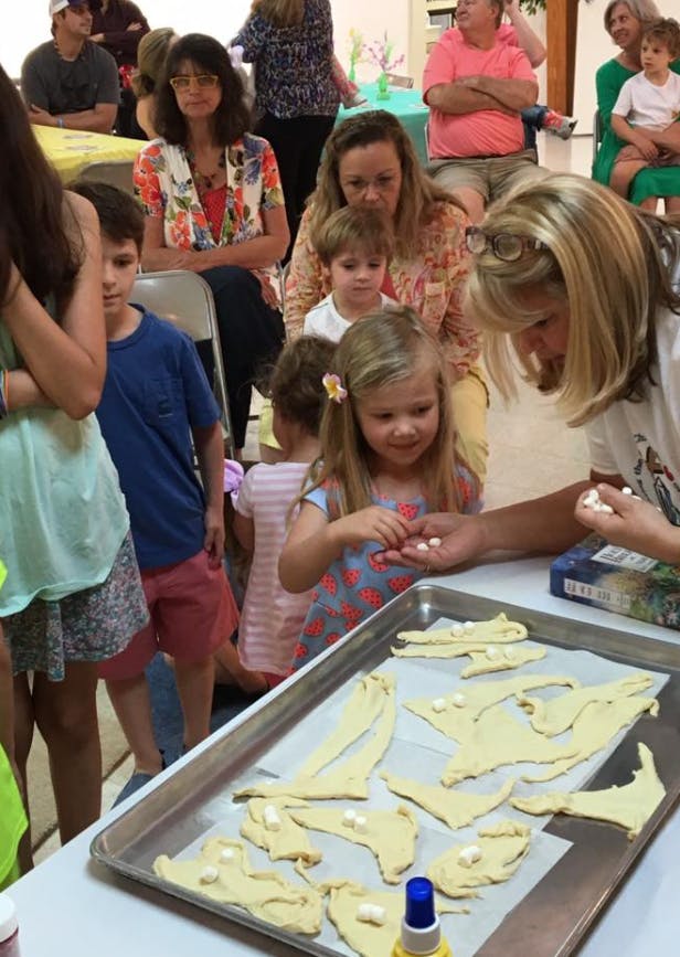 Adult and child placing small white candies on dough shapes on a baking sheet