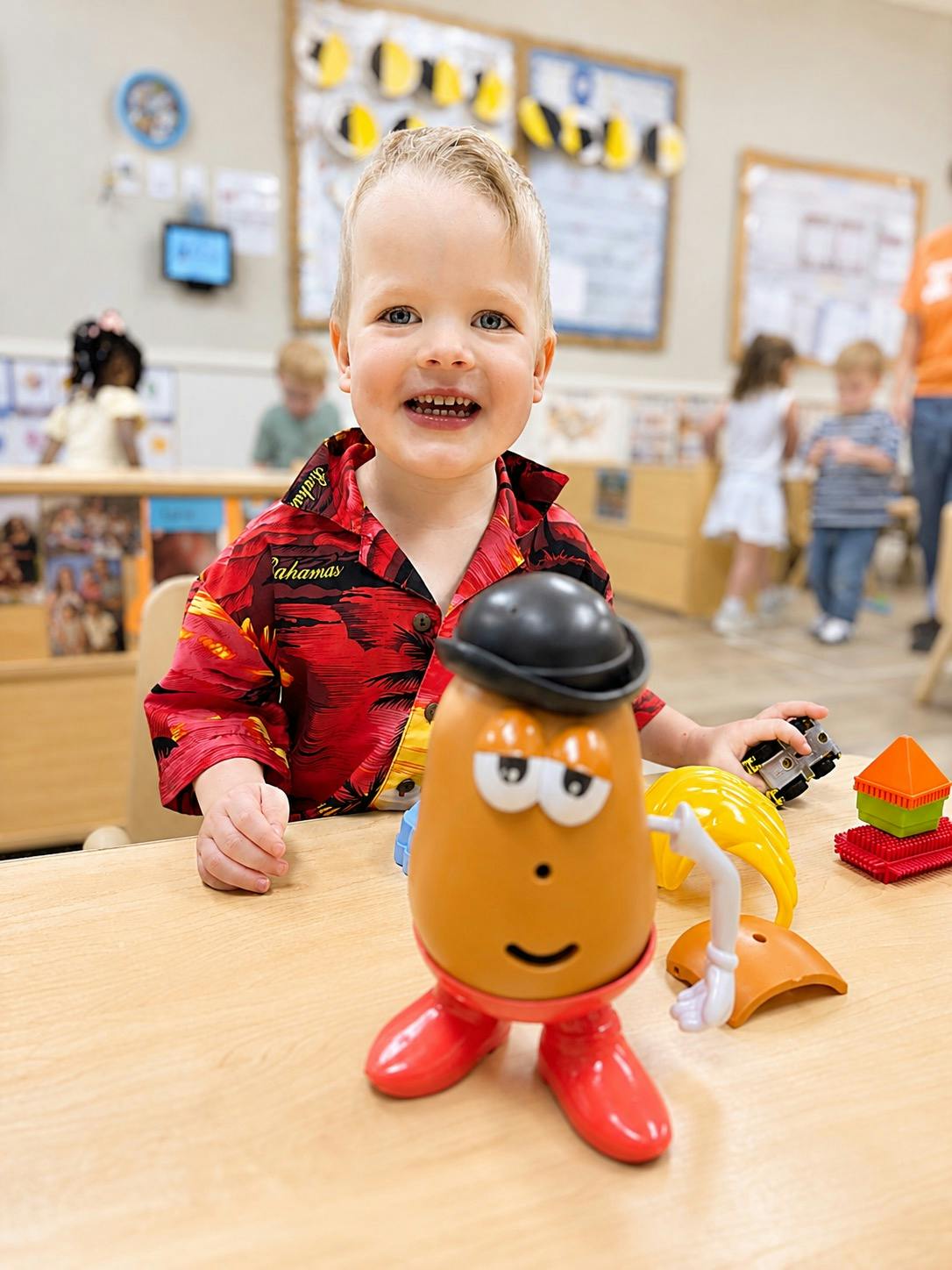 Child playing with a plastic potato toy at a table in a classroom