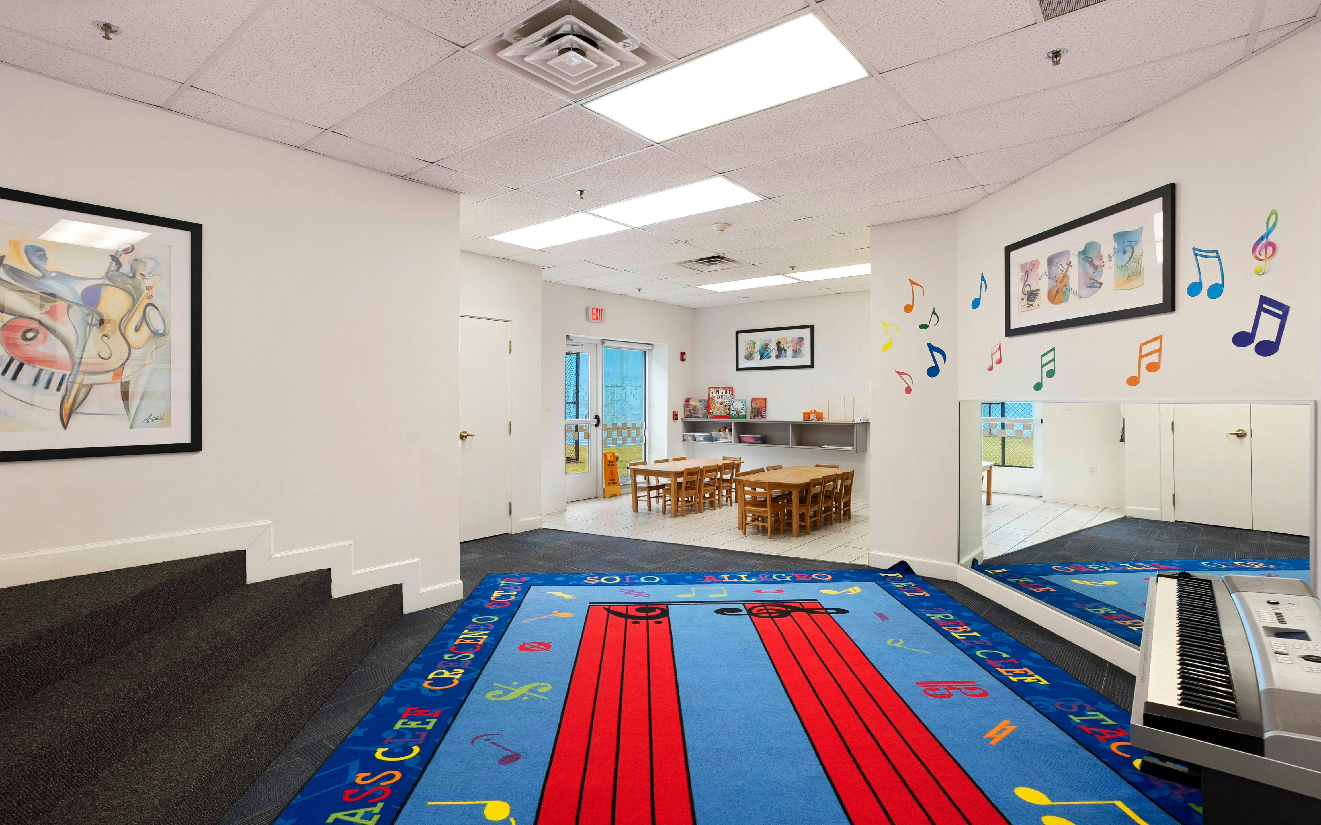 Music-themed playroom with a blue rug, small tables, and musical art on the walls