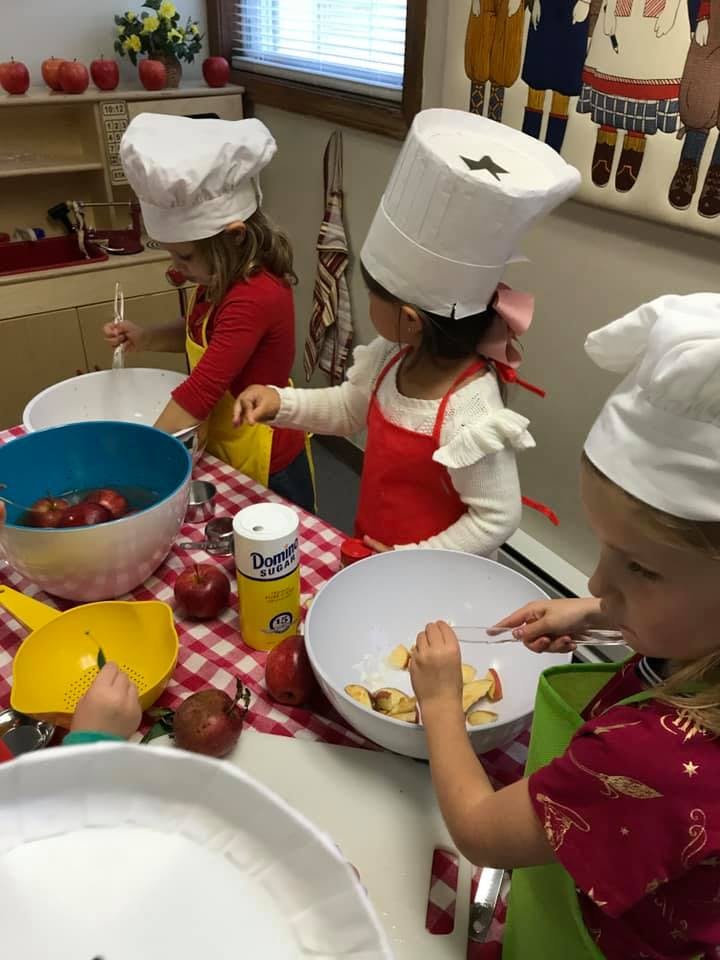 Children in chef hats and aprons preparing food in a classroom