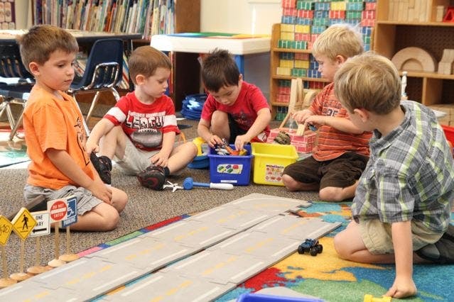 Five children playing with toys on the floor in a classroom