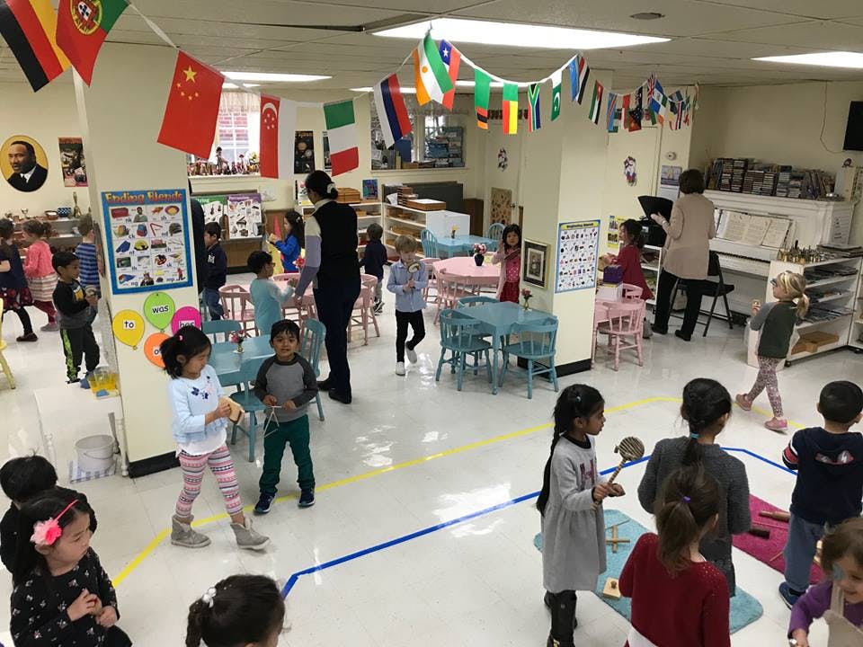 Many children and adults in a classroom with flags hanging