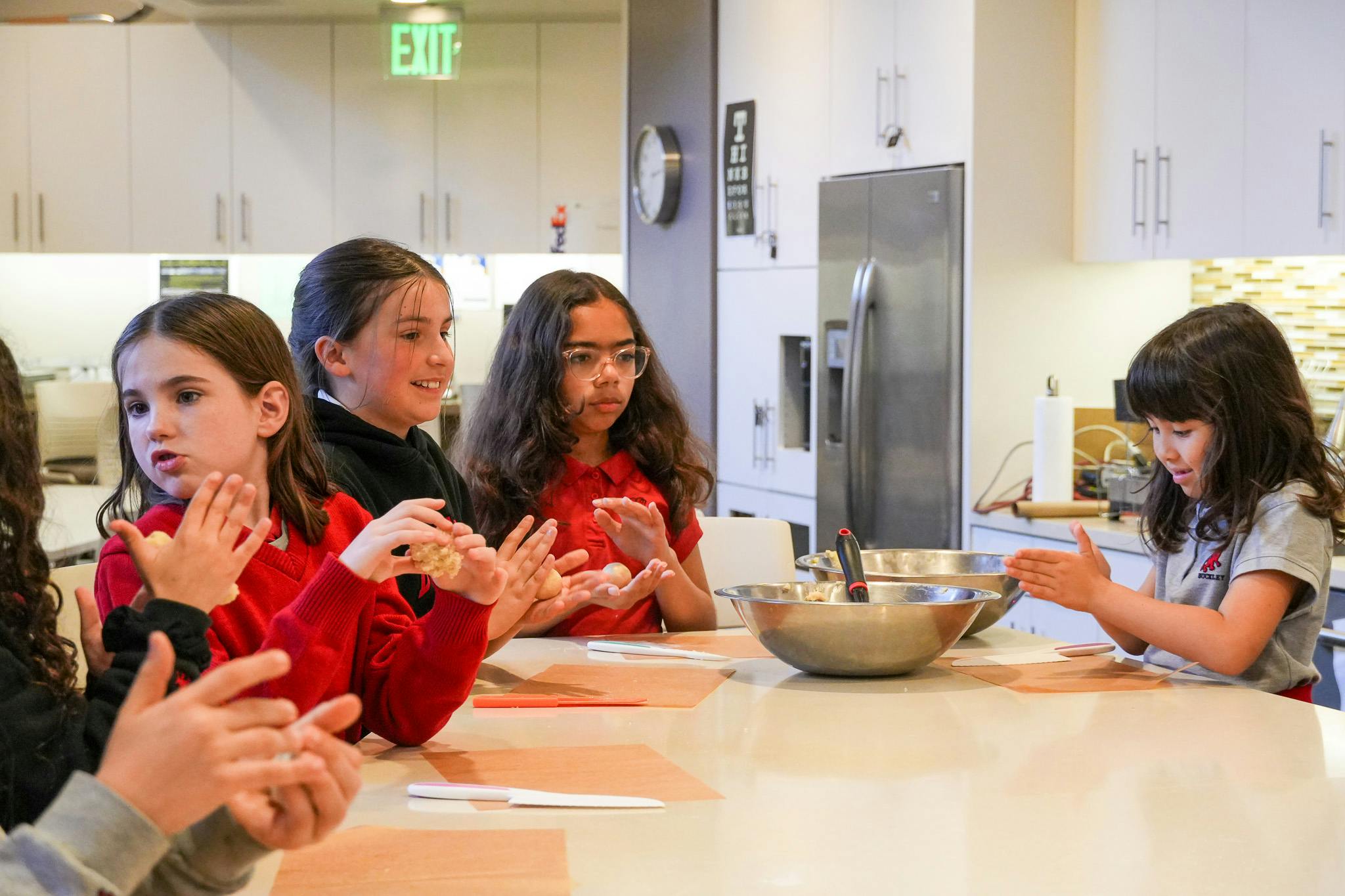 Children forming dough balls at a table in a kitchen