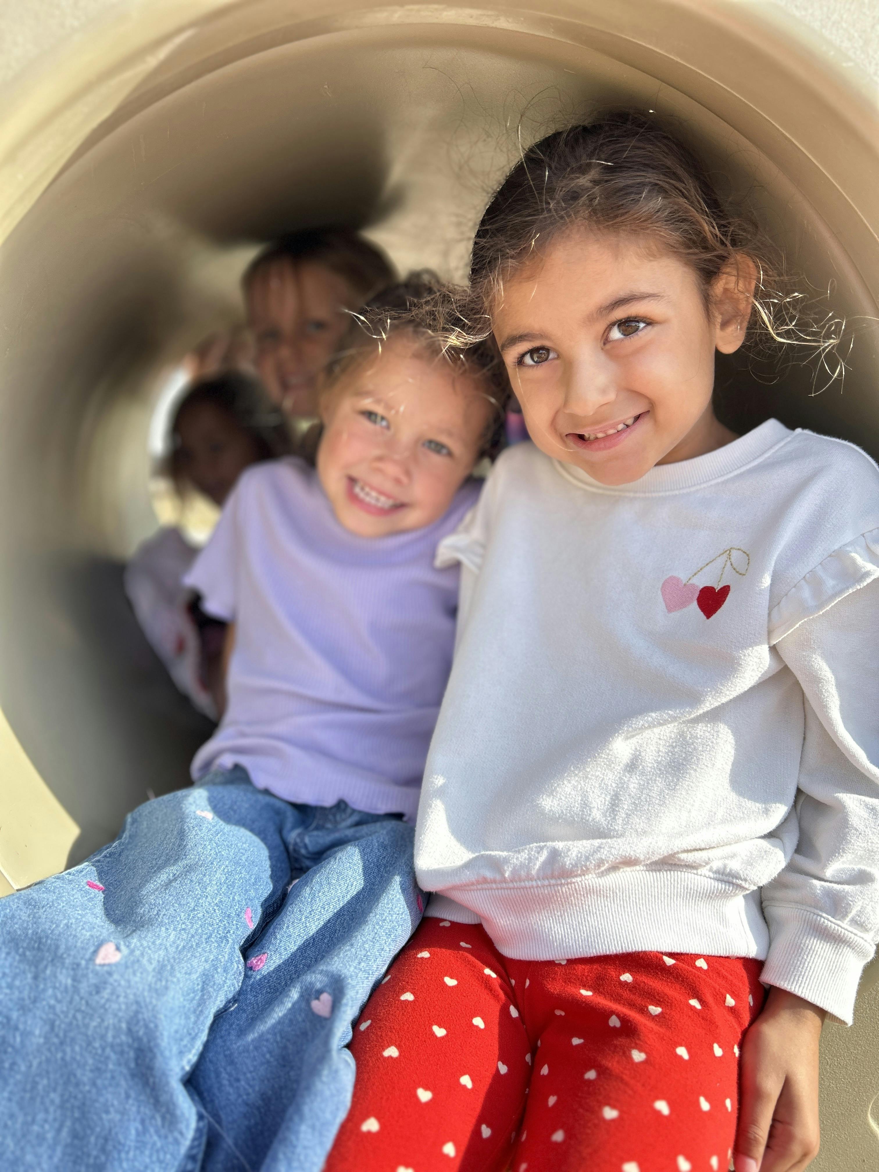 Two children smiling in a tunnel, with other children in the background