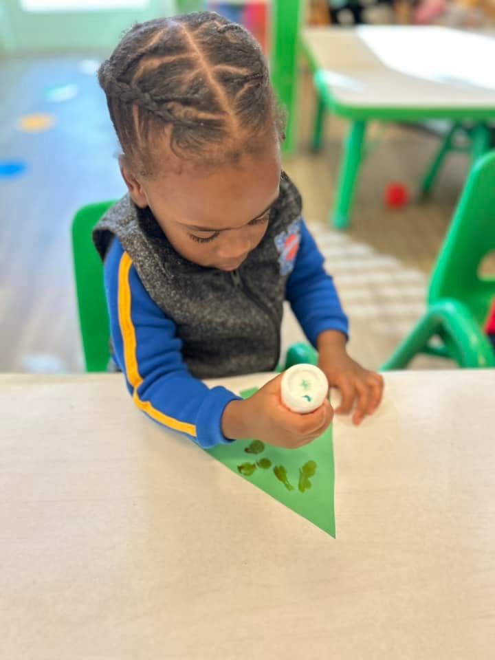 Child making art with green paper and paint in a classroom