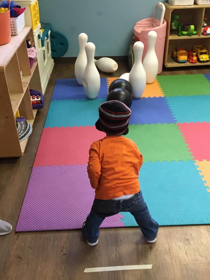 Child playing with bowling pins and balls on a colorful mat