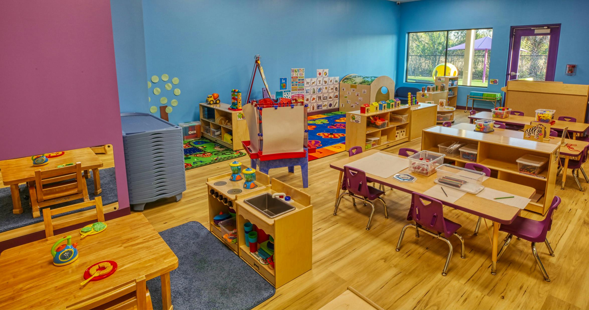Colorful preschool classroom with child-sized tables, chairs, and play areas