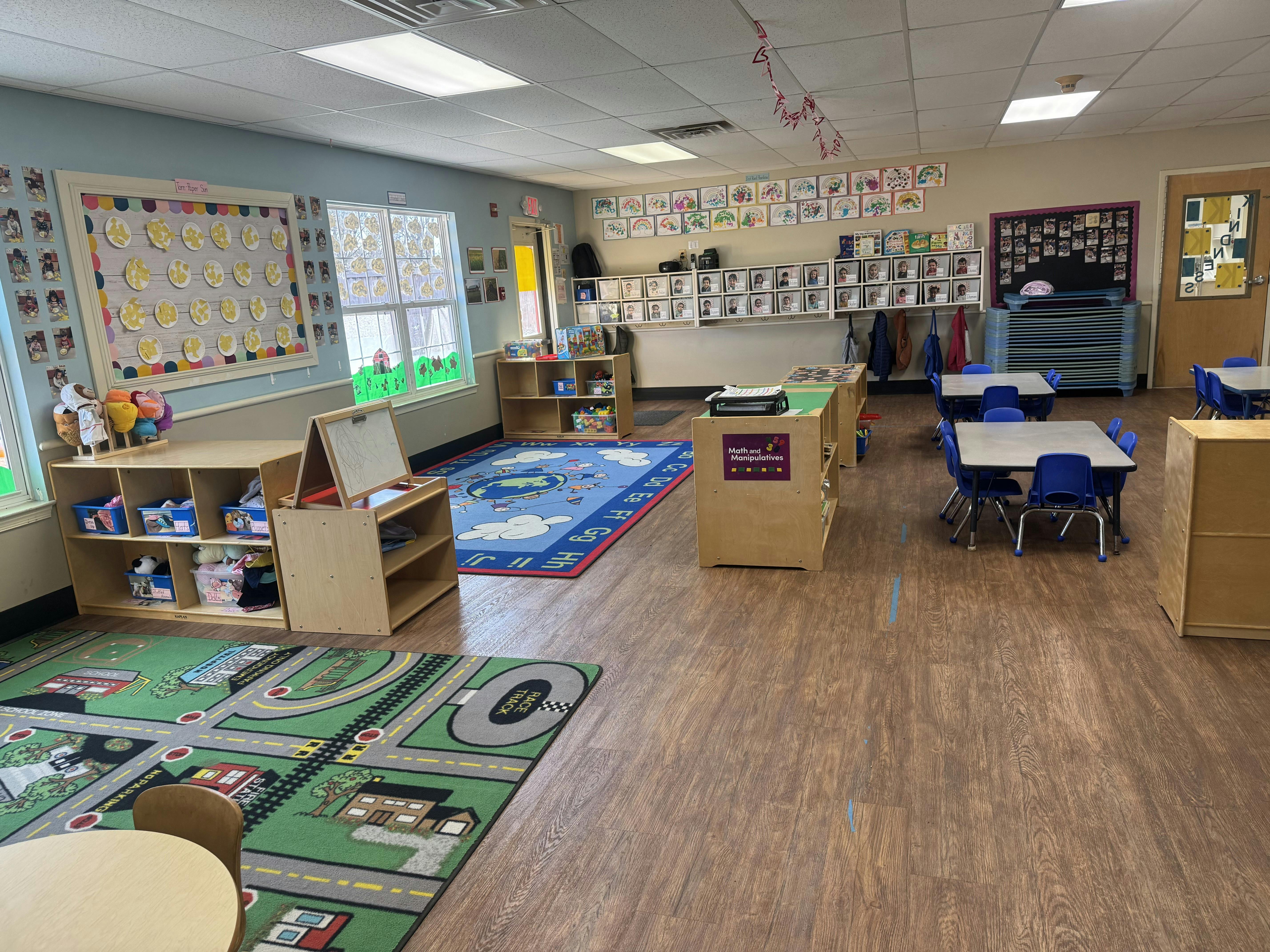 A colorful classroom with child-sized tables and chairs, shelves, and rugs