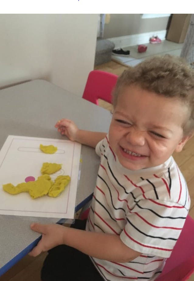 Child at a table with yellow playdough on a paper
