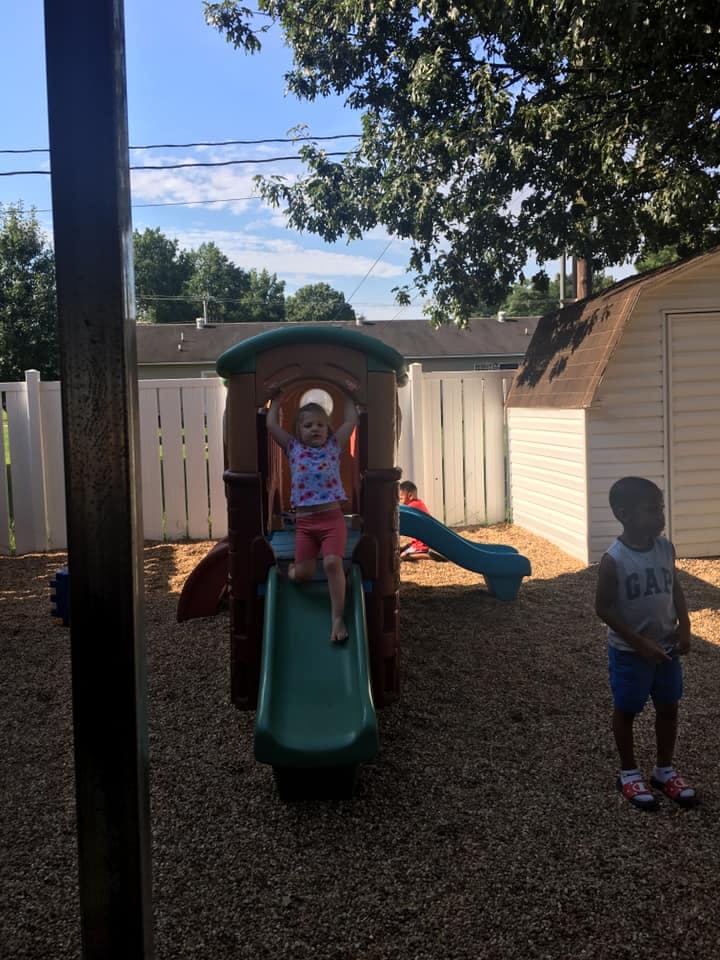 Child on a playground slide with another child standing nearby