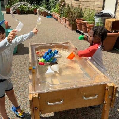 Two children playing with water and plastic toys at a wooden water table