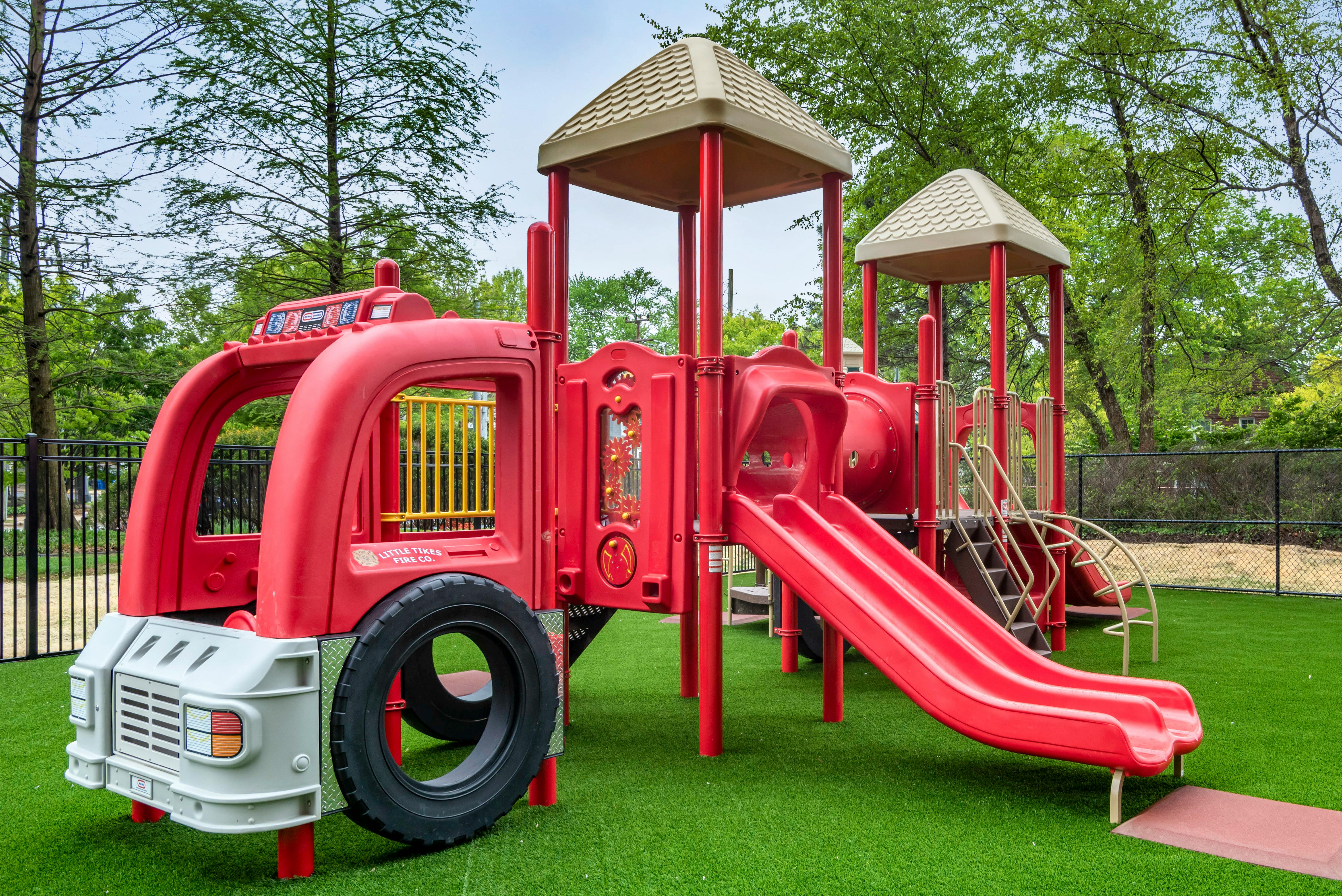 Red fire truck-themed playground with slide and play structures on green turf