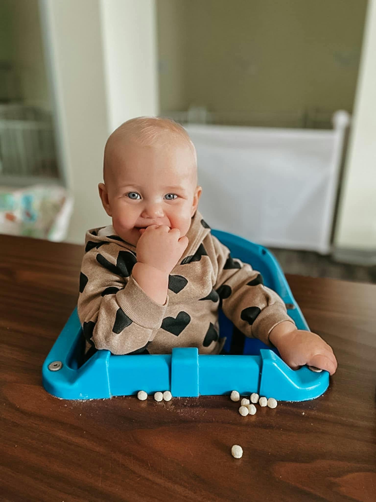 Child in a high chair with small white objects on the table