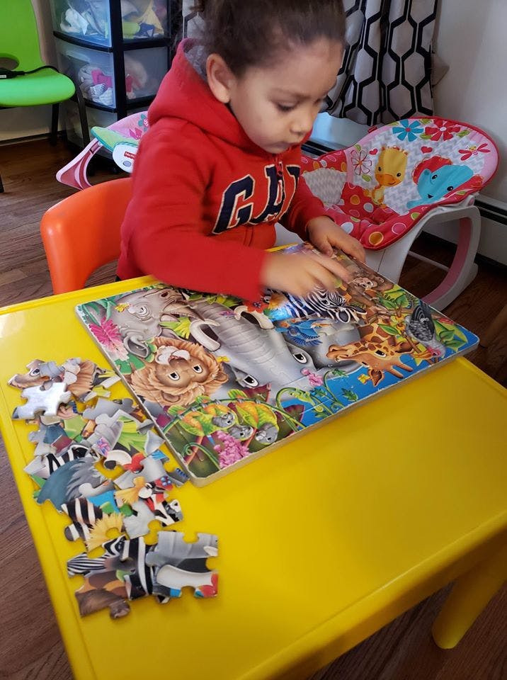 Child in a red hoodie playing with a puzzle on a yellow table
