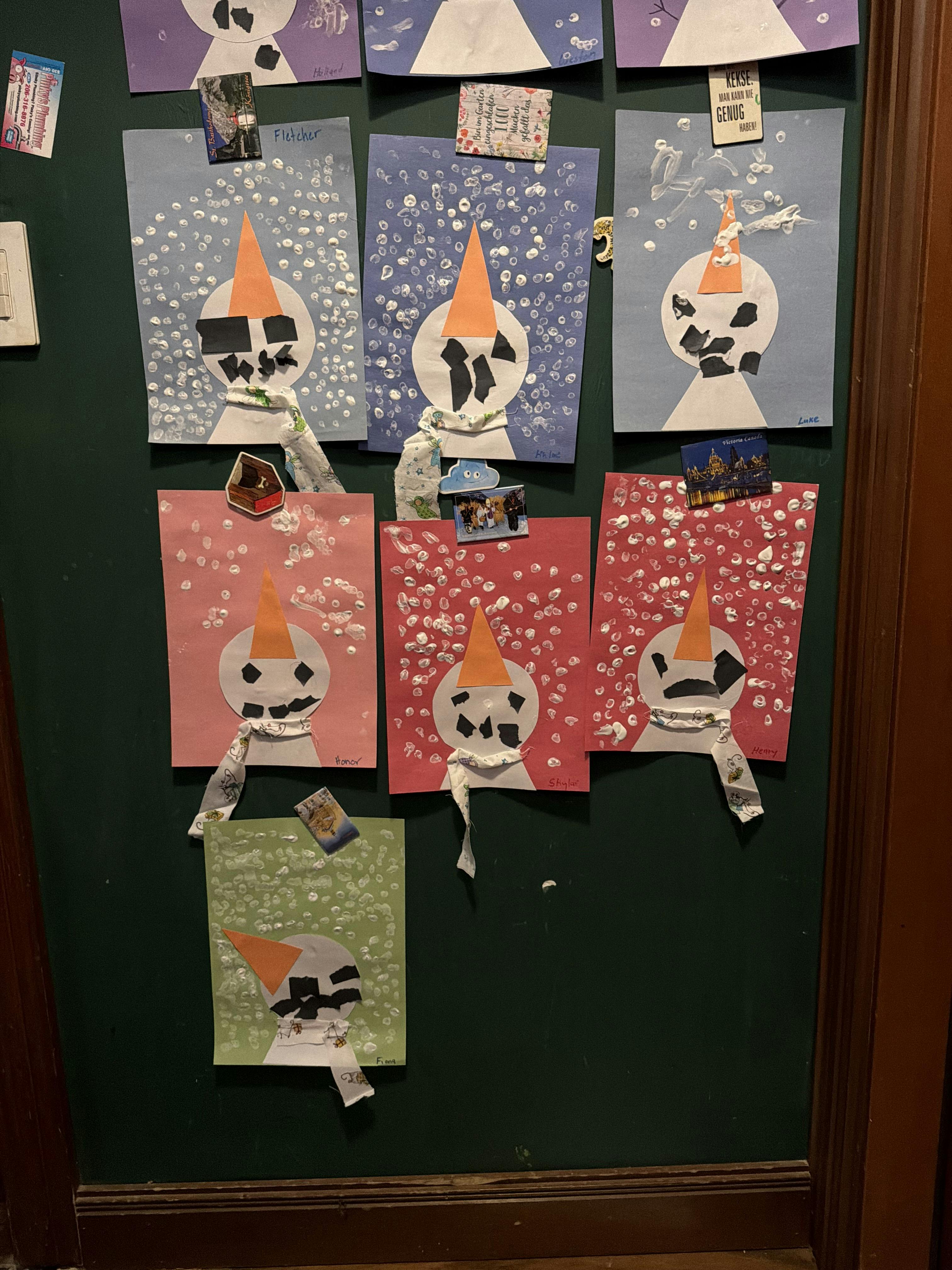 Child snowman crafts displayed on a green wall