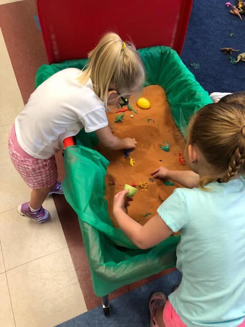 Two children playing with sand and small toys in a sensory bin