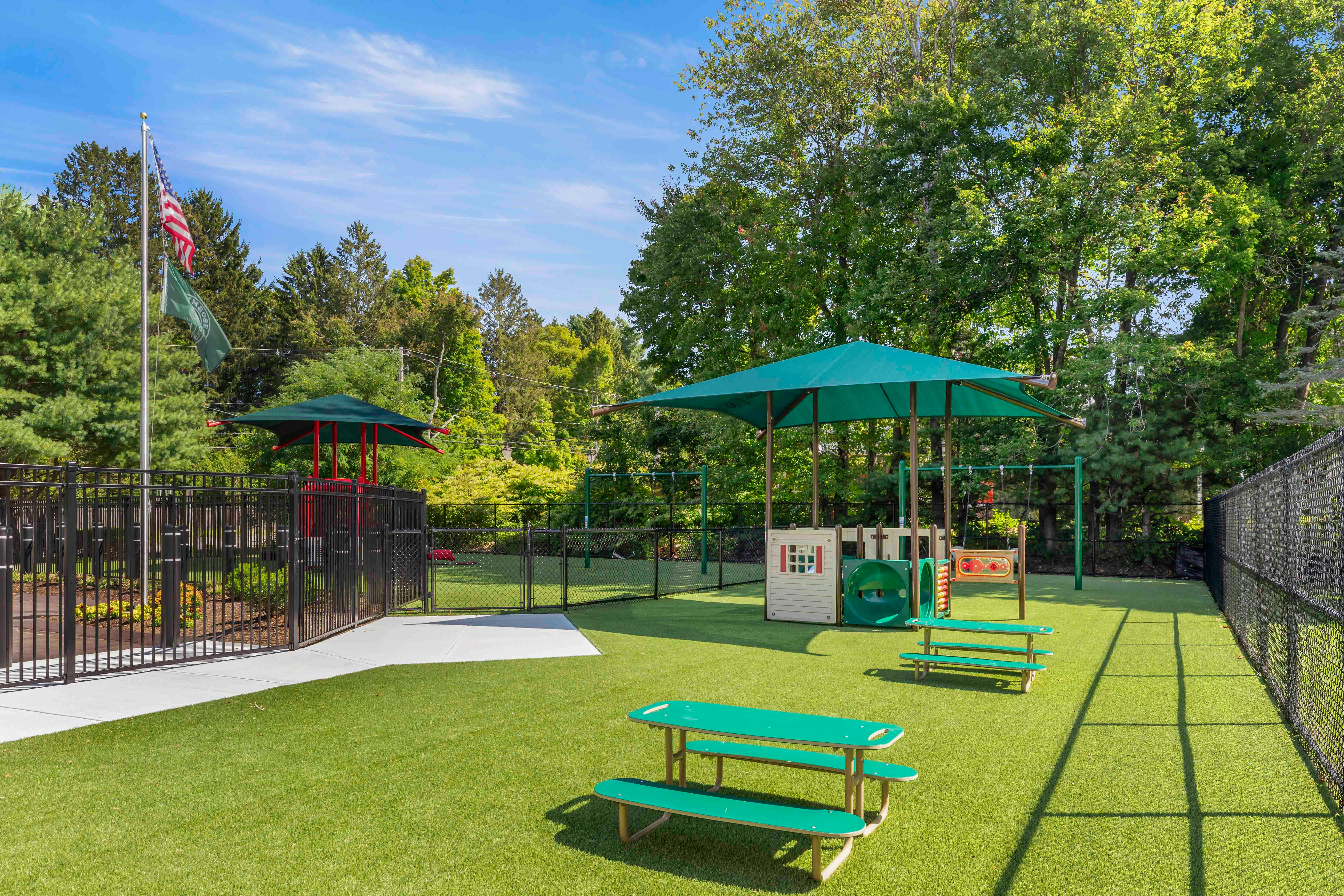 Outdoor playground with green turf, play structures, and picnic tables under awnings
