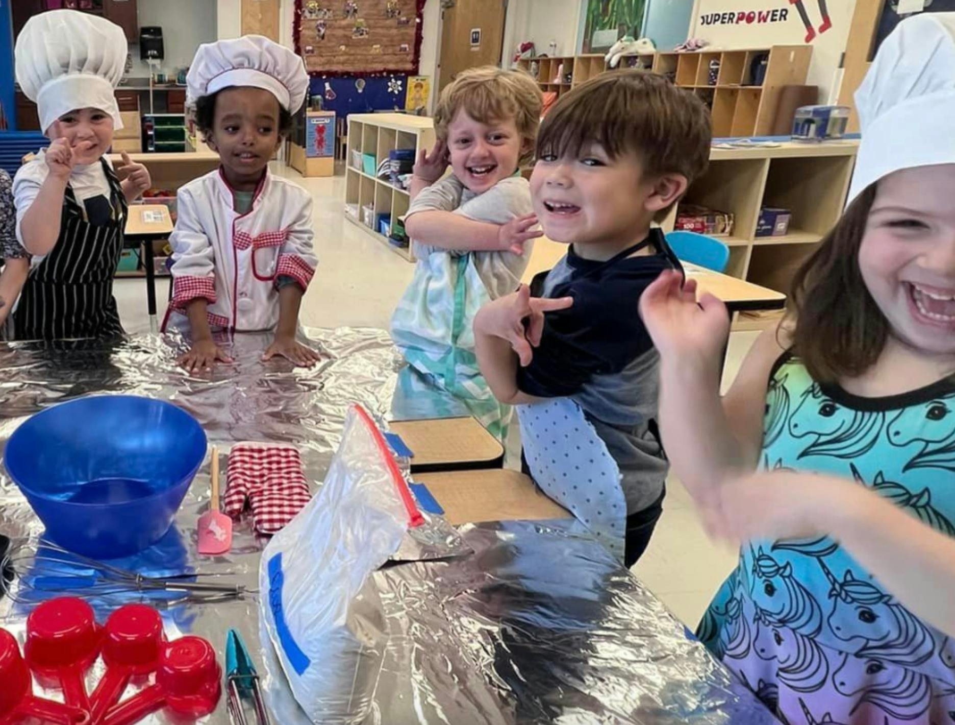 Children in chef hats and aprons at a table with cooking supplies