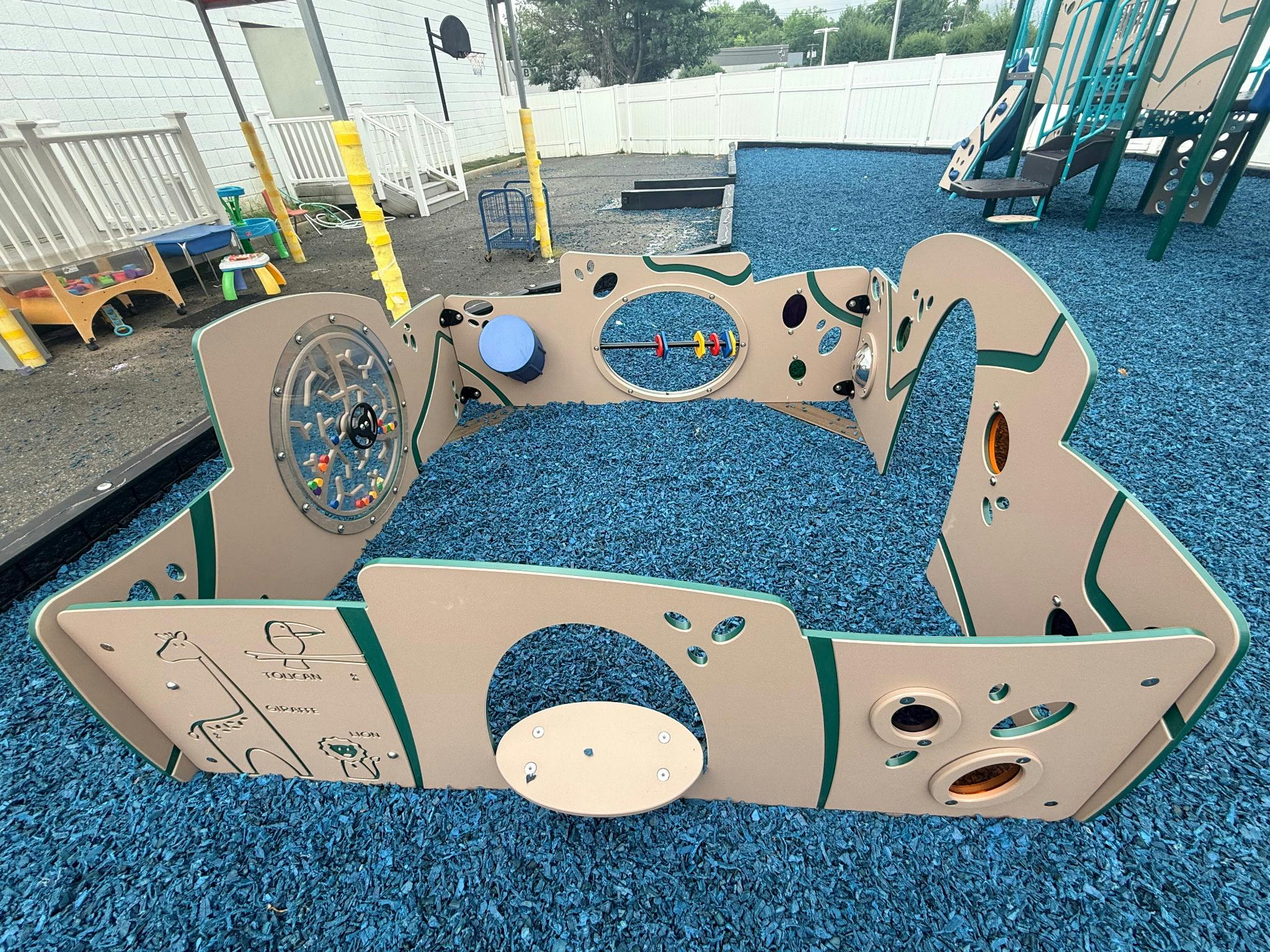 Playground area with an enclosed activity wall on blue rubber mulch