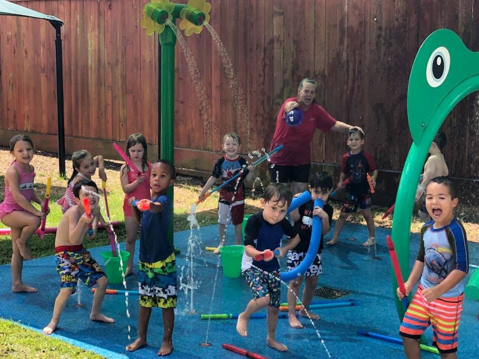 Children and an adult playing in a splash pad with water spraying