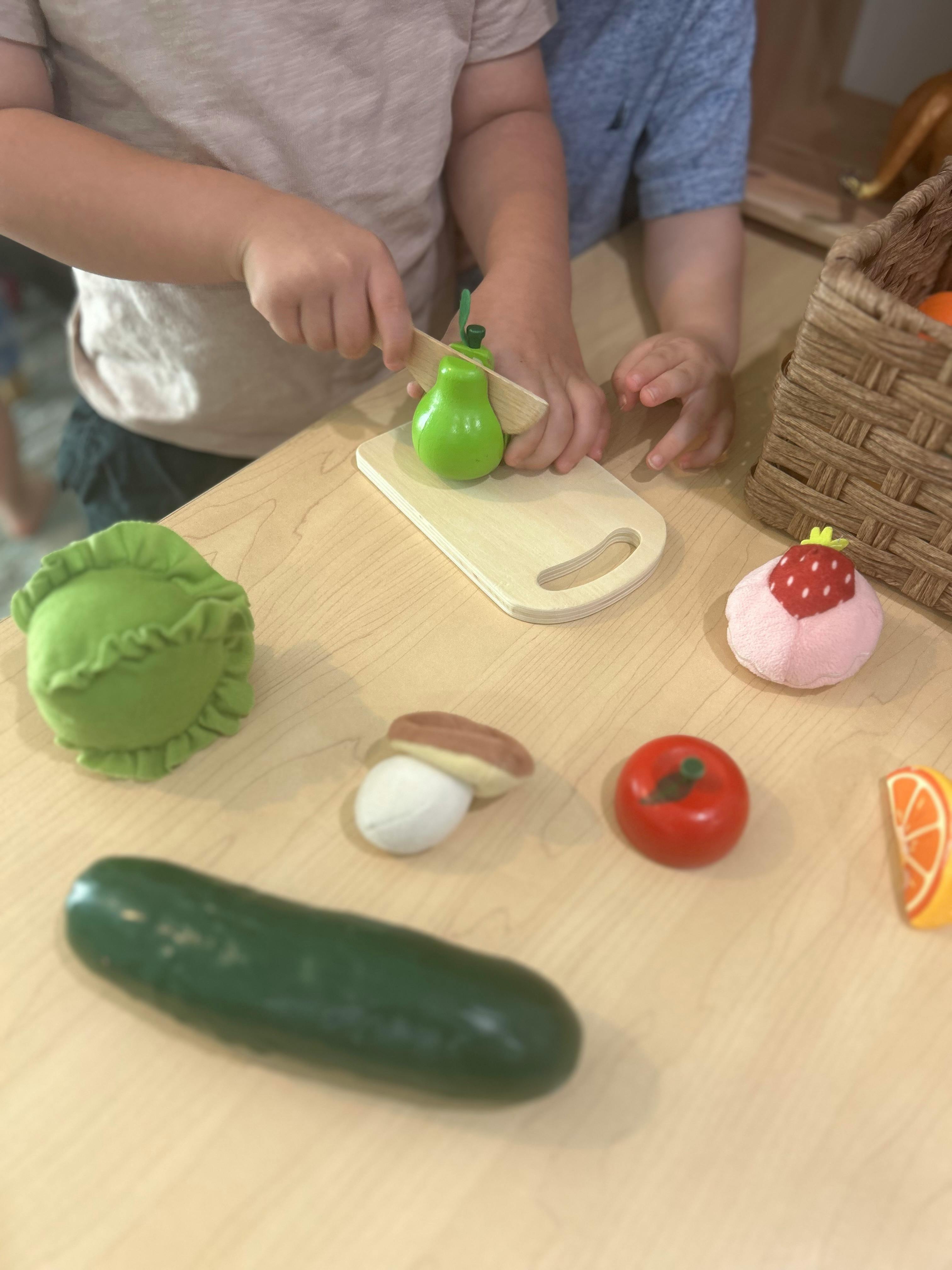 Child playing with toy food, cutting a green pear on a cutting board