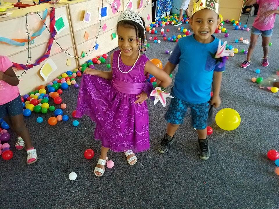 Two children in crowns holding hands, surrounded by colorful balls